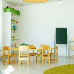 Sala colorida de educação infantil com mesas, cadeiras e materiais pedagógicos.