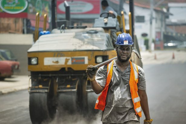 Trabalhador com equipamento de segurança atua em uma obra de pavimentação de rua.