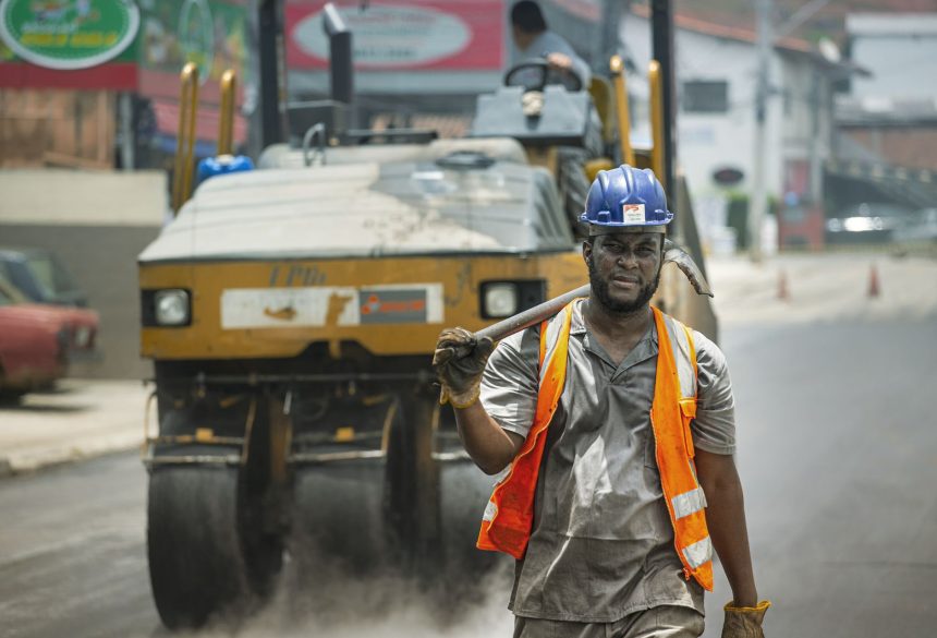 Trabalhador com equipamento de segurança atua em uma obra de pavimentação de rua.
