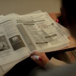 Pessoa consulta anúncios de emprego em um jornal e marca uma oportunidade com caneta.