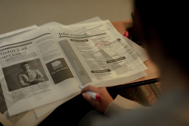 Pessoa consulta anúncios de emprego em um jornal e marca uma oportunidade com caneta.