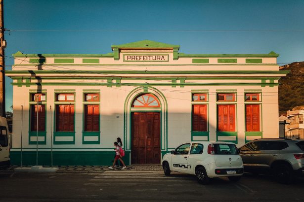 Prédio histórico de uma prefeitura brasileira, com fachada colorida e pessoas circulando ao entardecer.
