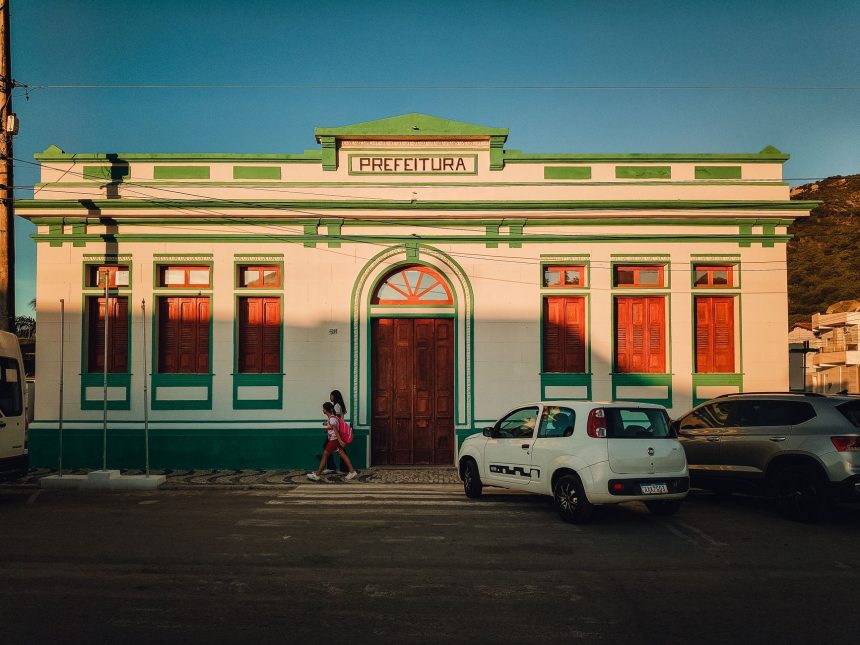 Prédio histórico de uma prefeitura brasileira, com fachada colorida e pessoas circulando ao entardecer.