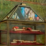 Vitrine ornamentada com relíquias religiosas em uma igreja, com reflexos de vitrais ao fundo