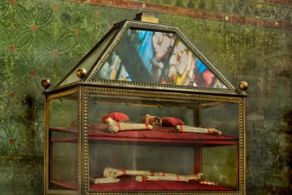 Vitrine ornamentada com relíquias religiosas em uma igreja, com reflexos de vitrais ao fundo