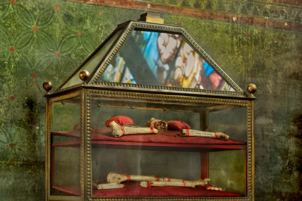 Vitrine ornamentada com relíquias religiosas em uma igreja, com reflexos de vitrais ao fundo