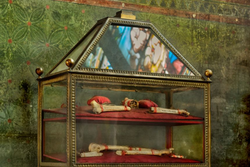Vitrine ornamentada com relíquias religiosas em uma igreja, com reflexos de vitrais ao fundo