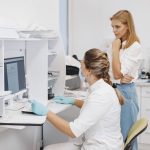 Duas profissionais de saúde analisam resultados de exames em um computador dentro de uma clínica.