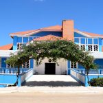 Fachada azul de um prédio público sob céu claro, vista de baixo para cima.