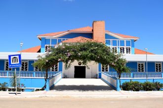 Fachada azul de um prédio público sob céu claro, vista de baixo para cima.