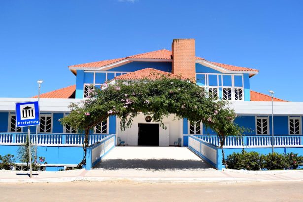 Fachada azul de um prédio público sob céu claro, vista de baixo para cima.