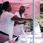 Duas mulheres vendem produtos a uma cliente em uma barraca de feira ao ar livre.