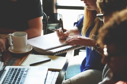 Grupo de pessoas reunido em uma mesa, discutindo anotações e planejando um projeto com notebooks e documentos.
